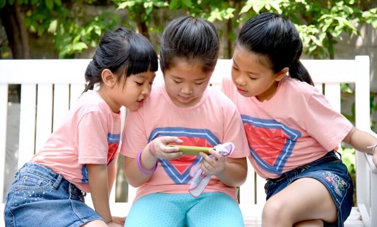 three young girls look at a smartphone