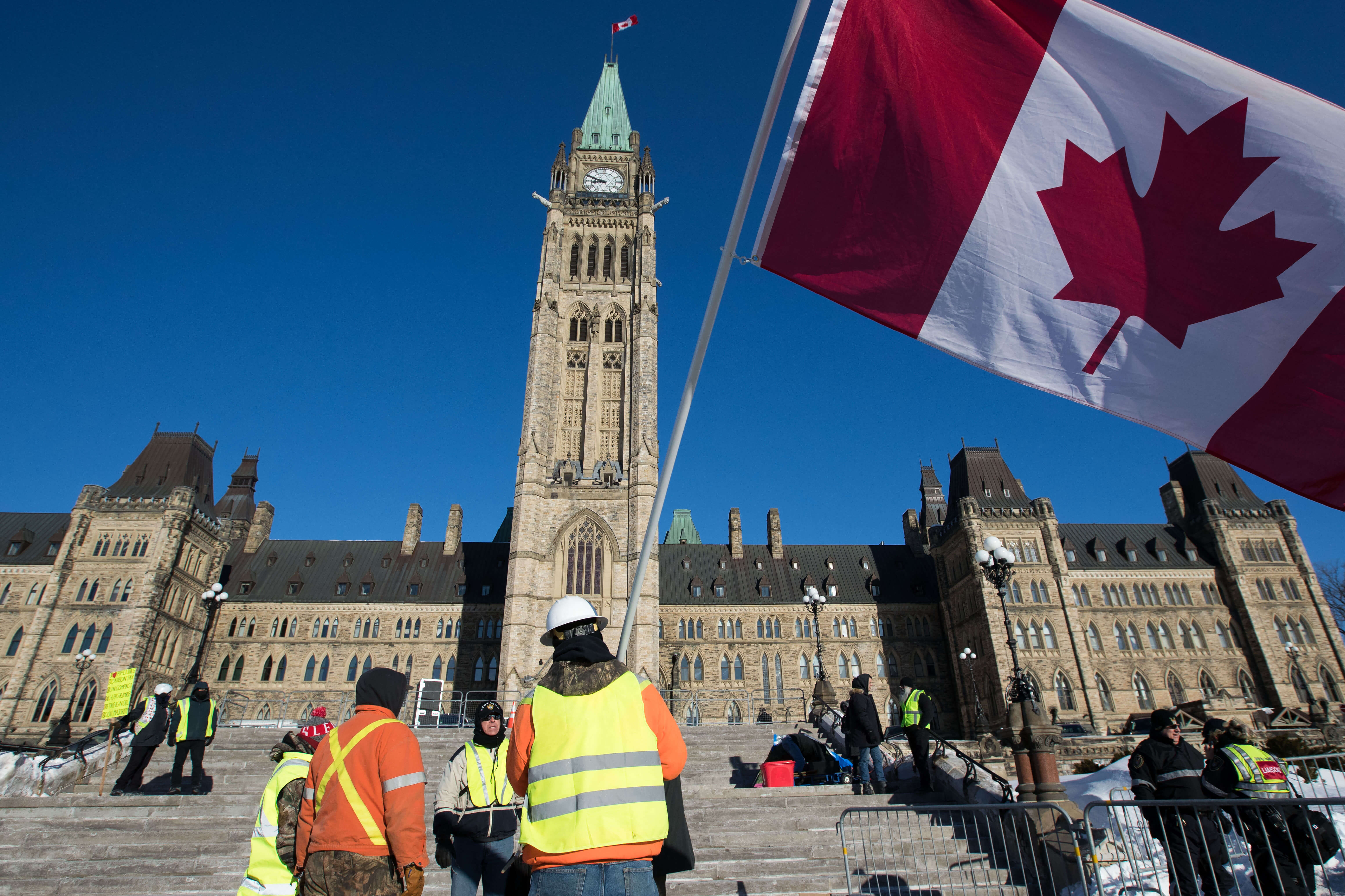 Canadian study permit rules: Two men are waving the Canadian flag in front of the parliament building in Ottawa