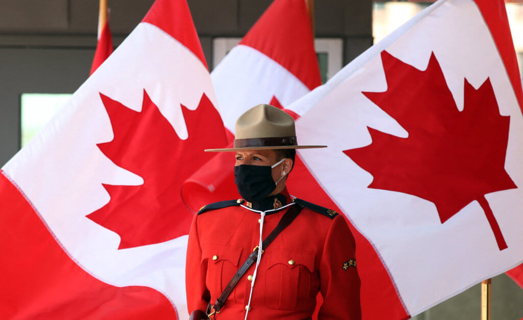 Canadian immigration: A female officer of the Royal Canadian Mounted Police force stands in front of a row of Canadian flags