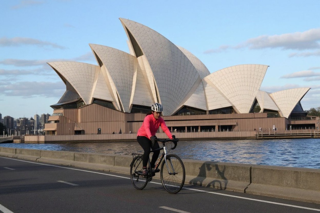 A student rides on a bicycle in front of the landmark Sydney Opera House. Source: