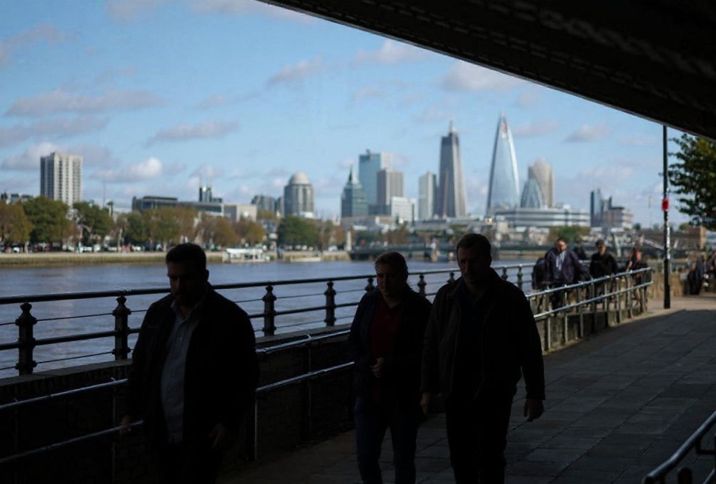 People walk along the River Thames with the City of London financial district in the distance on October 3, 2023. (Photo by HENRY NICHOLLS / )