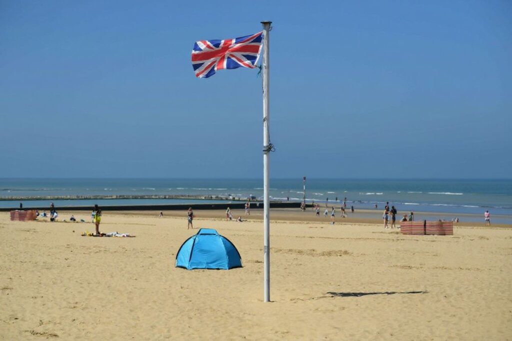 A Union flag flutters in the breeze as sunbathers take advantage of the fine weather on the beach on the coast at Margate. Source: Ben Stansall/