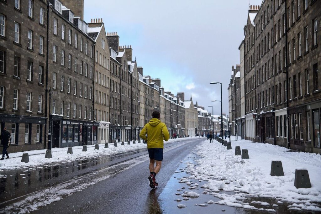 A jogger runs in the snow on the Royal Mile in Edinburgh on February 10, 2021. – Cold weather swept across northern Europe bring snow and ice. (Photo by Andy Buchanan / )