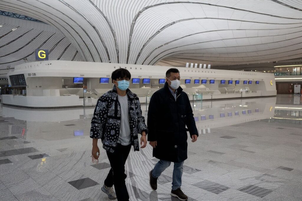 This picture taken on February 14, 2020 shows two men wearing face masks walking through a nearly empty terminal at Daxing international airport in Beijing, as travel has ground to a halt in the wake of the the COVID-19 coronavirus outbreak. Source: NICOLAS ASFOURI/