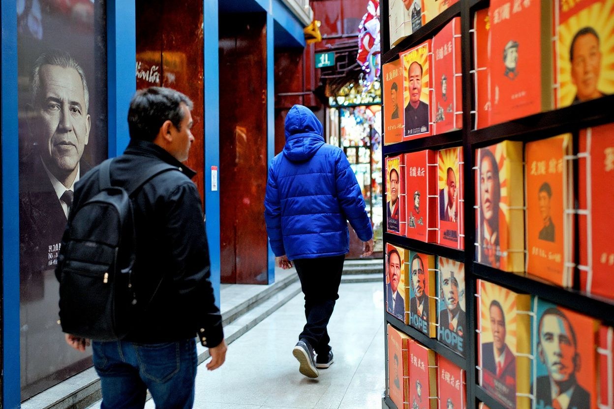 A foreigner walks past notebooks printed with portraits of late Chinese Communist leader Mao Zedong (L) and acting president of the United States Barack Obama (C) in Shanghai on February 10, 2010.  Sino-US tensions have increased in the past weeks with the latest rows surfacing over the value of the Chinese yuan and the Dalai Lama’s upcoming visit to the White House.   PHOTO / PHILIPPE LOPEZ (Photo by PHILIPPE LOPEZ / )