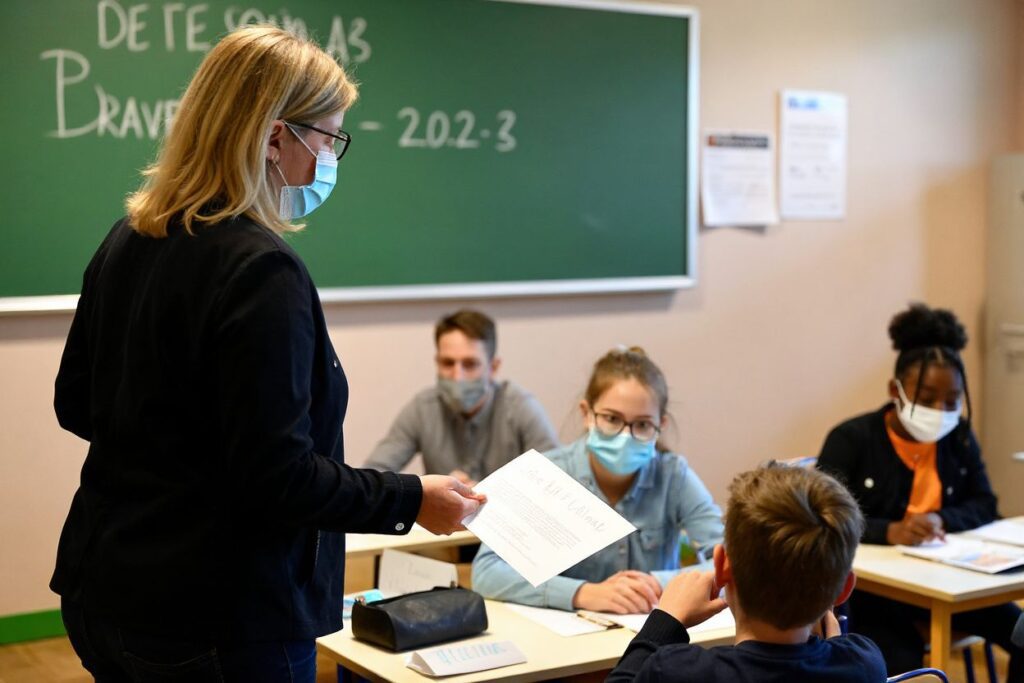 (FILES) In this file photo taken on September 01, 2020 a teacher with a protective mask distributes documents to pupils in a classroom in Brequigny high school in Rennes, western France, on the first day of the school year amid the Covid-19 epidemic. – The debate on whether or not to open schools is raging and fuelled by new strains of the Covid-19 coronavirus, of which the effect on children is still poorly understood. The World Health Organization continues to recommend that every effort should be made to avoid mass closures. “School closures should be a last resort, they should be temporary and only at a local level in areas of intense transmission” of the Covid-19 giving virus, the WHO repeats in a chapter of its weekly epidemiological report, devoted to lessons learned from a year of pandemic in education. (Photo by Damien Meyer / )