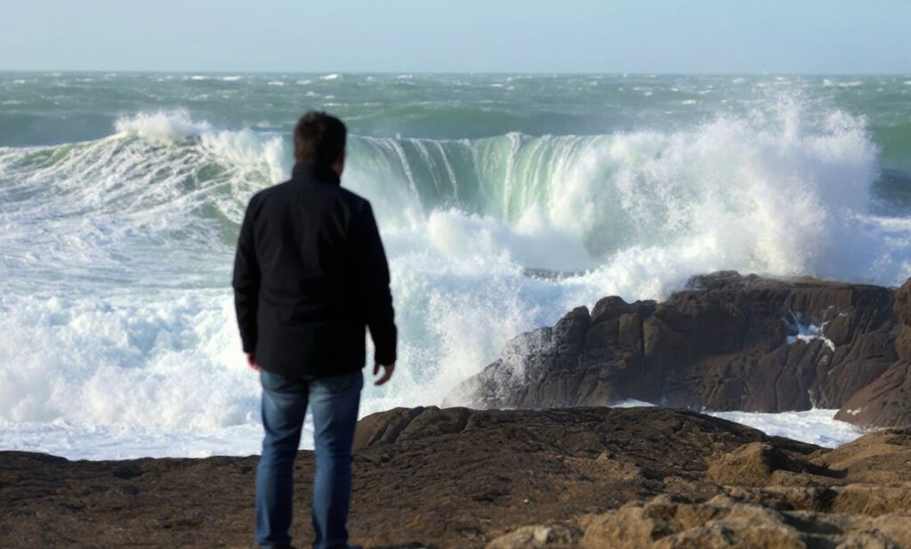 A man stands on rocks watching the crashing waves of the Atlantic ocean at Saint-Guénolé,  western of France on February 13, 2016. (Photo by FRED TANNEAU / )