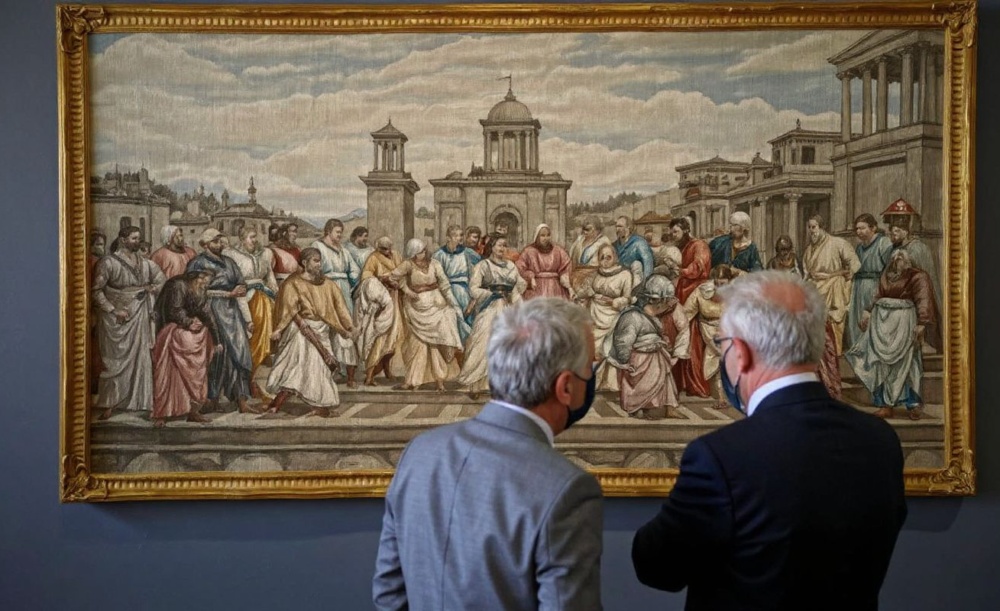 Two men look at a tapestry depicting “The School of Athens during its official presentation at the Greek Parliament on March 22, 2021. Source: Aris Messinis/