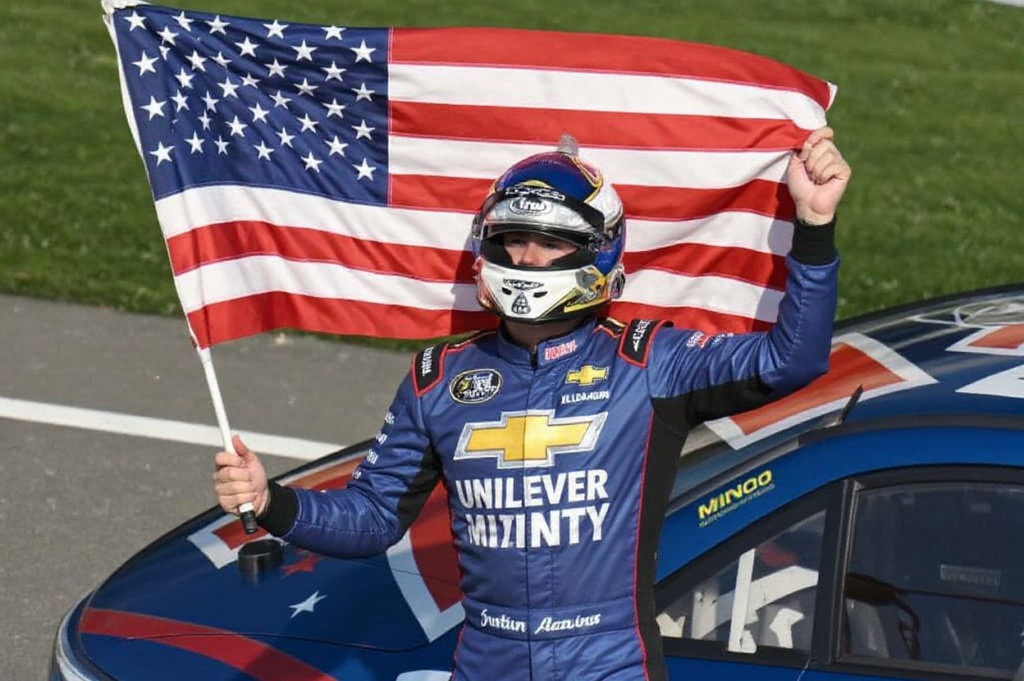 CONCORD, NORTH CAROLINA – MAY 29: Justin Allgaier, driver of the #7 Unilever Military DeCA RCPT Chevrolet, celebrates with the American flag after winning the NASCAR Xfinity Series Alsco Uniforms 300 at Charlotte Motor Speedway on May 29, 2023 in Concord, North Carolina.   Logan Riely/Getty Images/ (Photo by Logan Riely / GETTY IMAGES NORTH AMERICA / Getty Images via )