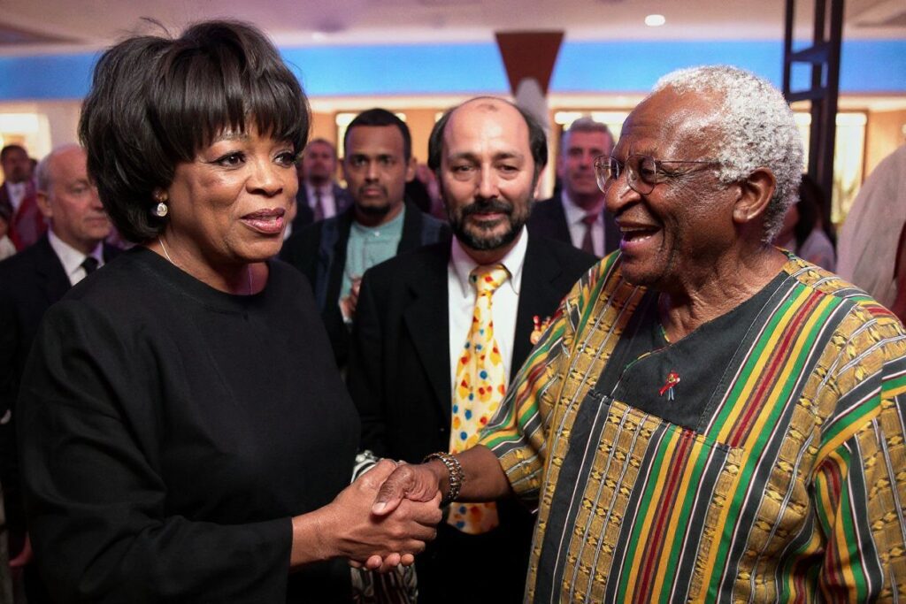 (FILES) In this file photo taken on December 18, 2000 US Television talk show host Oprah Winfrey greets former South African anti-apatheid icon and Archbishop Desmond Tutu (R). Winfrey met Tutu during the opening of an independent movie house chain, owned by renowned producer Anant Singh, looking on in the background. – South African anti-apartheid icon Desmond Tutu, described as the country’s moral compass, died on December 26, 2021, aged 90, President Cyril Ramaphosa said. (Photo by )