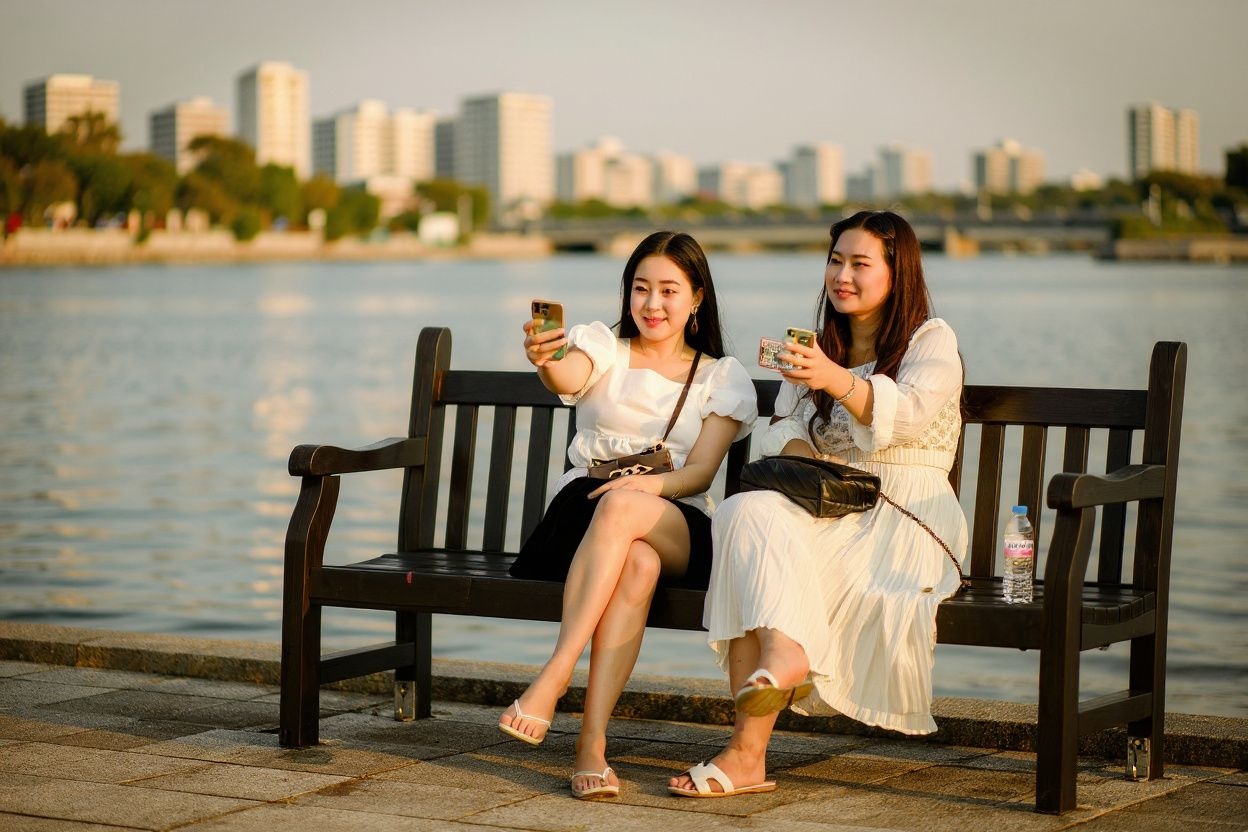 Women pose for selfies as they sit on a bench along the Han River in Seoul on September 15, 2021. (Photo by Anthony WALLACE / )