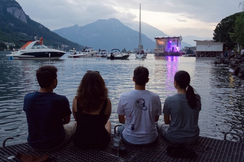 People watch the Lake Stage from the shore of Lake Geneva during a concert by Swiss band Annie Taylor at the opening of the Montreux Jazz Festival in Montreux on July 2, 2021. – After a 2020 edition cancelled due to the pandemic, the famous festival, which takes place on the shores of Lake Geneva in Switzerland, at the foot of the mountains, is eagerly awaiting the return of its public, who will have to carry a vaccination certificate for paying concerts. (Photo by Fabrice COFFRINI / )
