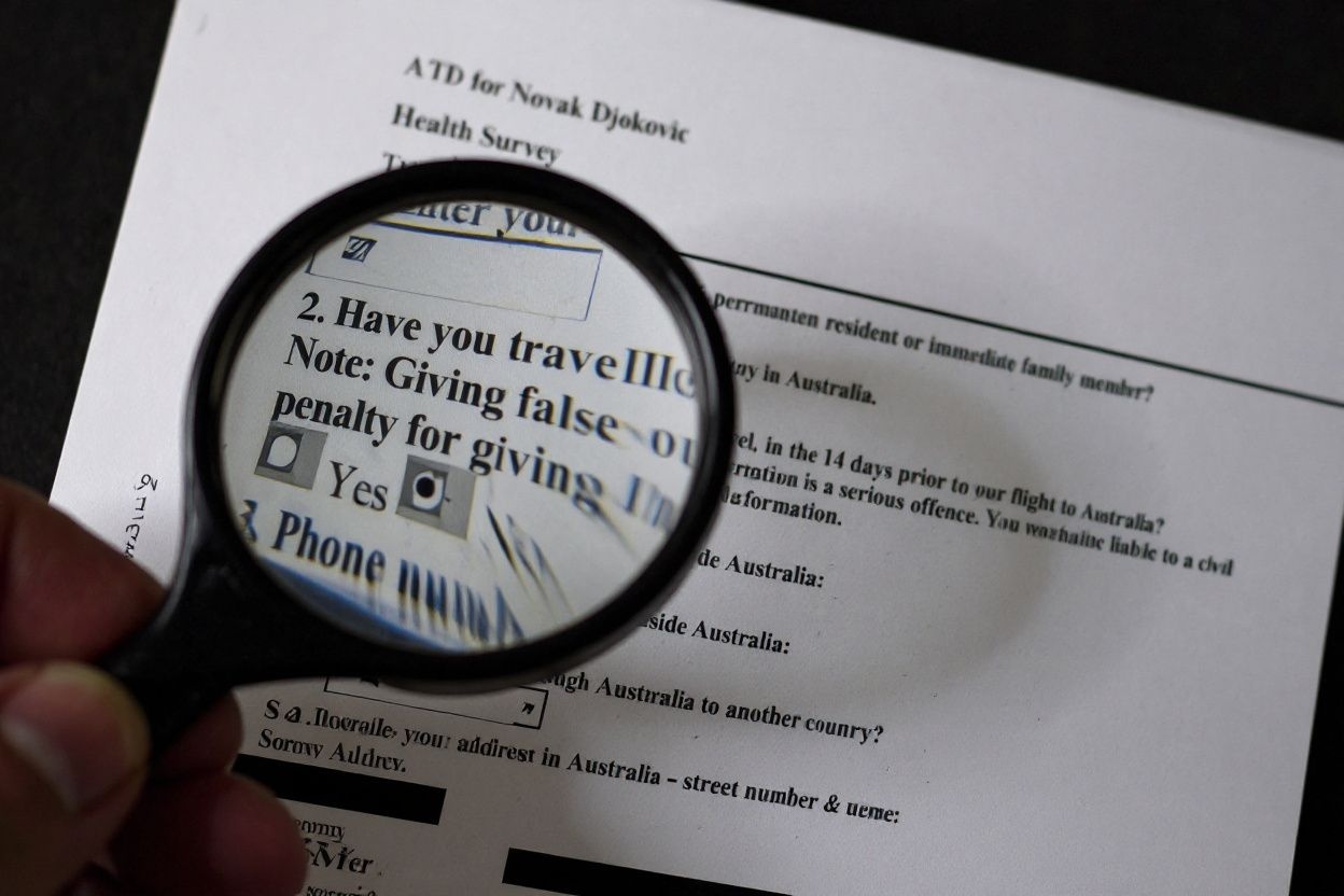 This photo illustration taken in Hong Kong on January 11, 2022 shows a magnifying glass highlighting a released copy of Serbian tennis champion Novak Djokovic’s health survey submitted during his Australian visa application process for his arrival in Melbourne ahead of the Australian Open tennis tournament. – Djokovic, who arrived in Melbourne on January 5, was released from detention on January 10 following a court ruling that overturned the cancellation of his Australian visa over his Covid-19 vaccination status. (Photo by Richard A. Brooks / )